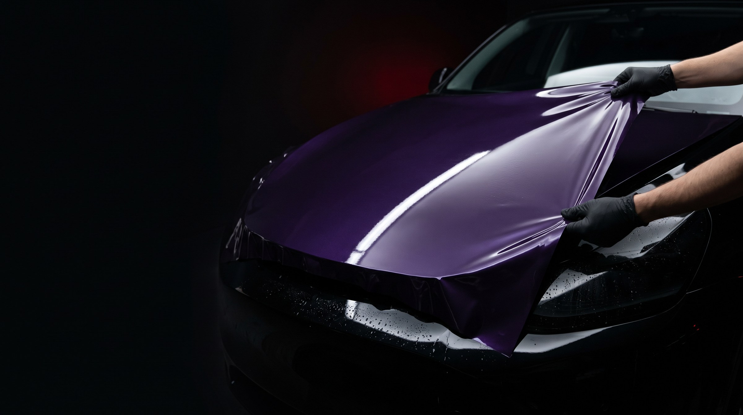 Gloved installer applying purple colour protection film to a car bonnet