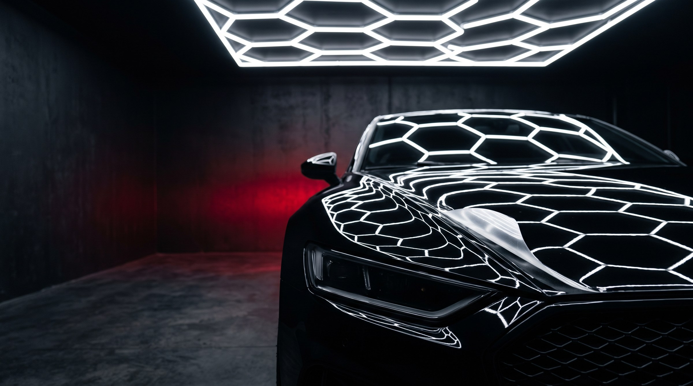 Black car with paint protection film in a hexagon-lit install bay